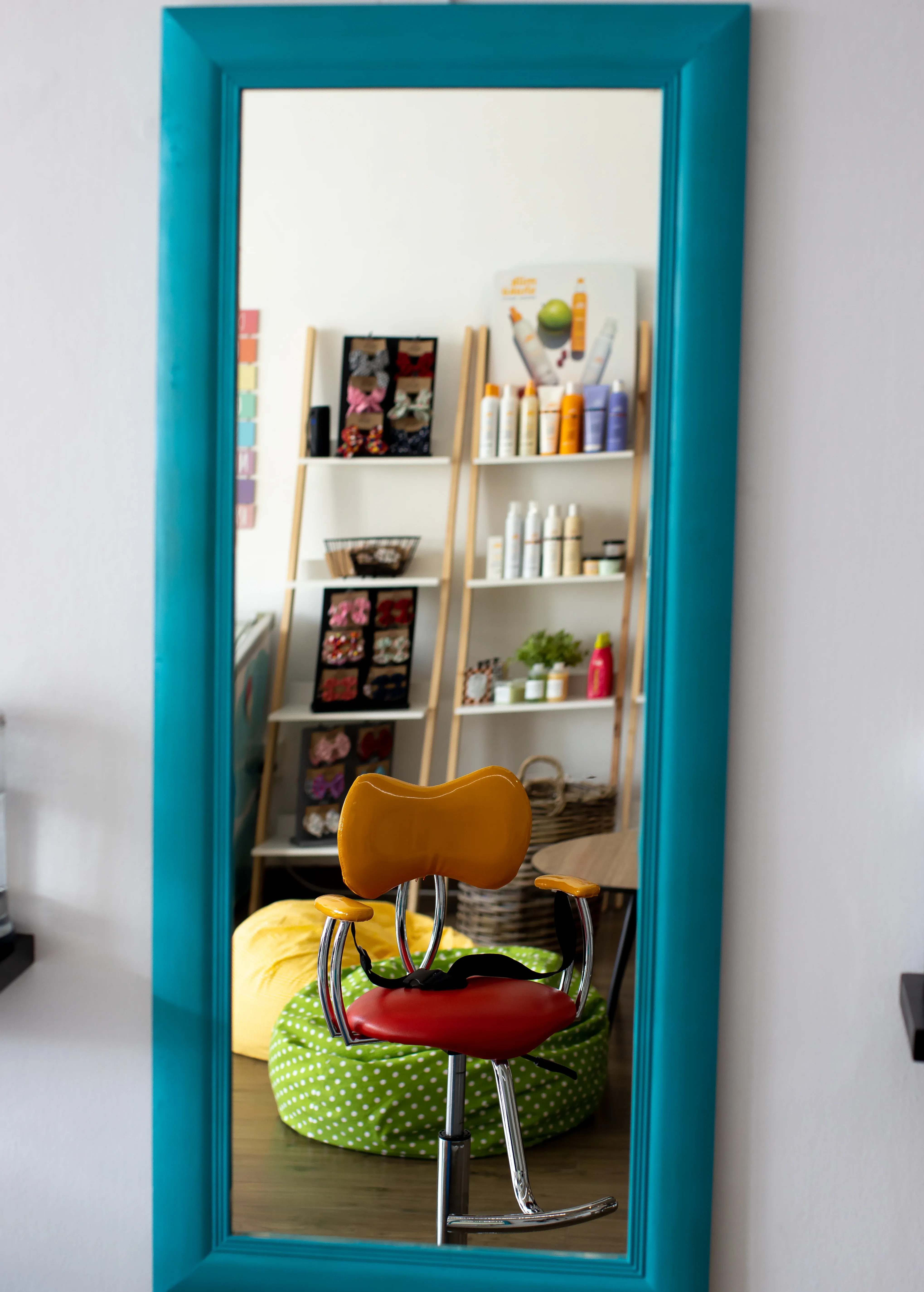 The teal mirror reflecting the salon interior — styling chair, product shelves and bean bags