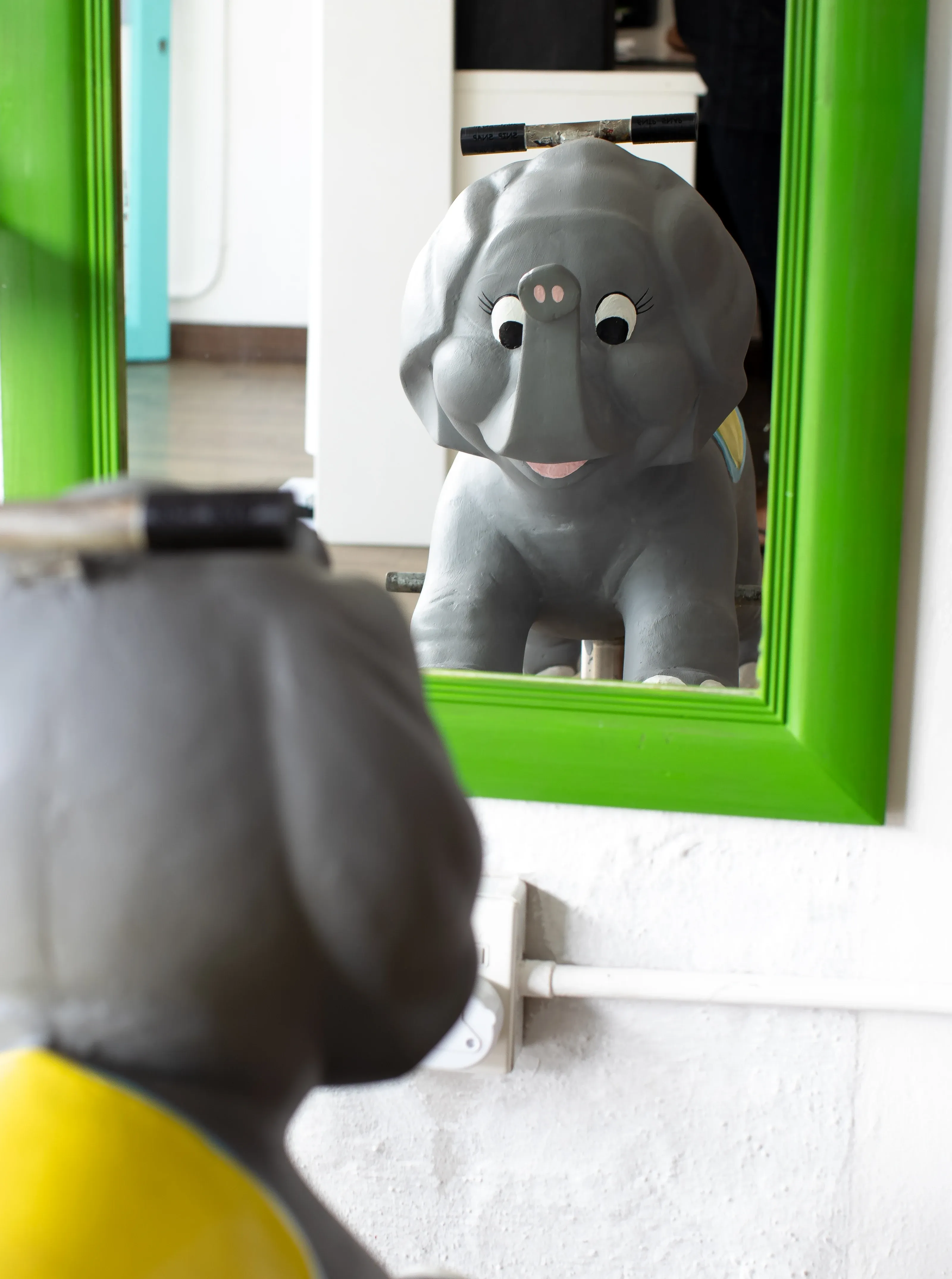 The elephant chair reflected in the green-framed salon mirror